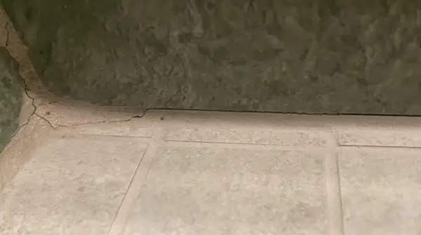 Pęknięta, biała masa między płytkami sugeruje, że szukamy co zamiast fugi. Zielona ściana nad nią.
