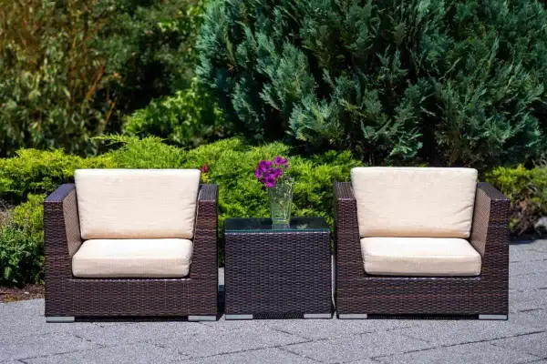 Dos sillones y una mesita de centro de ratán, perfectos para el mantenimiento de muebles de exterior. Flores moradas en un jarrón.