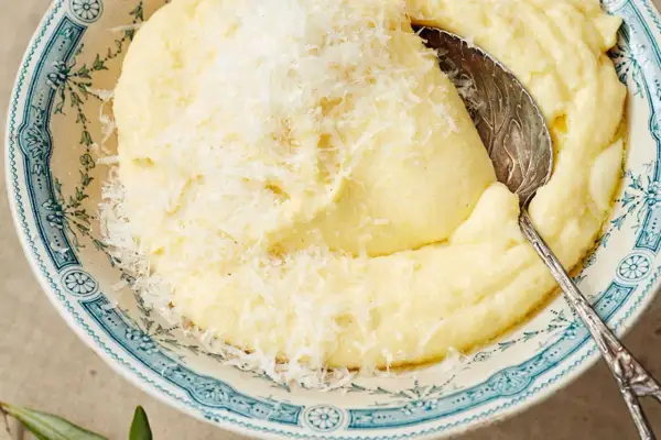 Cremige Polenta, frisch gekocht und mit Parmesan bestreut, wartet in einer blumig verzierten Schüssel auf den Löffel.