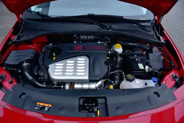 Silnik fiat bravo 1.4 t-jet w komorze pod maską. Widoczny akumulator, układ dolotowy i osłona silnika.