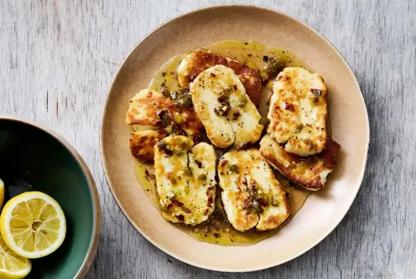 Stekt, marinerad halloumi med en kryddig dressing och chiliflakes. Serveras på en tallrik med citronklyftor vid sidan.