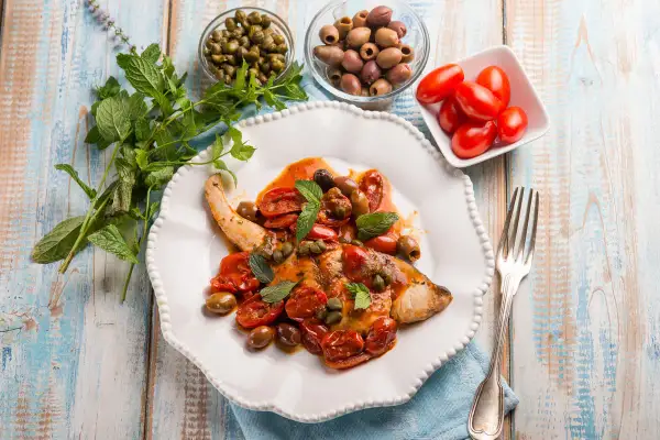 Un saporito pesce spada alla siciliana, condito con pomodorini, olive, capperi e menta fresca, pronto per essere gustato.