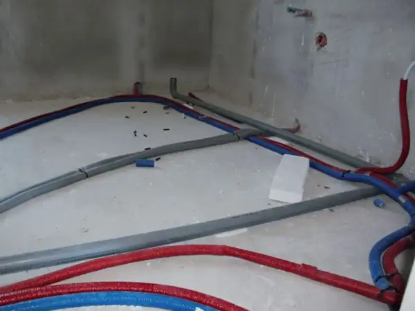 Na betonowej posadzce widać instalację wodną z czerwonych i niebieskich rur, które tworzą skomplikowany trojnik.