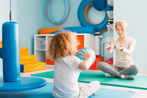Dziecko z kędzierzawymi włosami bawi się piłką sensoryczną, a terapeuta wyjaśnia, integracja sensoryczna co to jest.