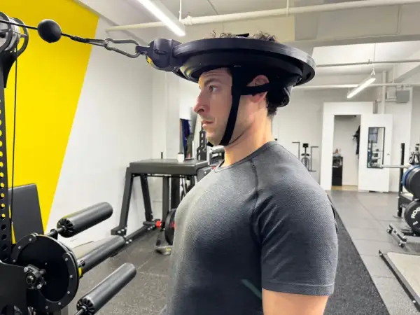 Man performing neck curls with a weighted harness in a gym.