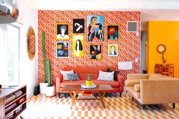 Vibrant living room with a bold 70s aesthetic. Orange patterned wallpaper, a cactus, and colorful art create a retro vibe.