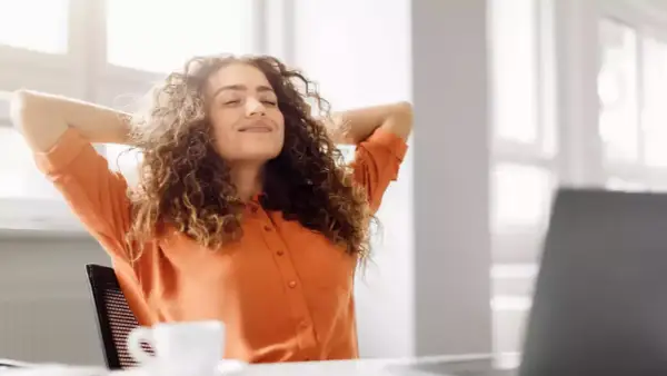 Femme souriante, mains derrière la tête, profitant d'une pause. Son retour congé maternité obligation employeur semble bien se passer.