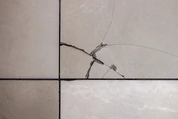 Gros plan sur un carrelage beige fissuré, montrant les étapes pour comment reparer un eclat de carrelage.