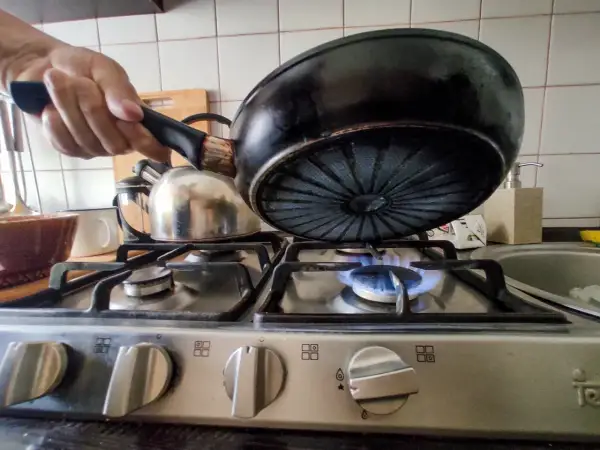 Gotowanie na małym ogniu to jeden ze sposobów, jak obniżyć rachunki za gaz. Patelnia nad płomieniem.