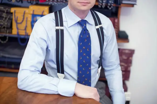 Elegancki mężczyzna w błękitnej koszuli, ozdobionej wzorem z ptakami, ma na sobie stylowe szelki i krawat.