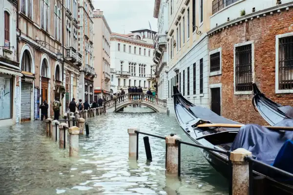 Venecia cuando se inunda: góndolas esperan en canales crecidos, peatones cruzan un puente sobre el agua que llega a las puertas de las tiendas.