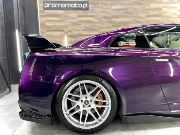 Sportowy Nissan GT-R w odcieniu **midnight purple**, z karbonowym spoilerem i felgami.