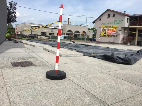Zabezpieczenie terenu budowy: czerwono-białe słupki i taśma ostrzegawcza oddzielają plac budowy od chodnika.