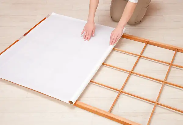 Mains déroulant du papier pour fabriquer une cloison japonaise sur un cadre en bois.