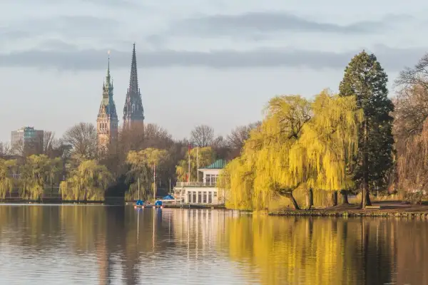 Ein idyllischer Blick auf den Alstersee in Hamburg. Sehens. Ein Bootshaus und die Türme der Stadt spiegeln sich im Wasser.