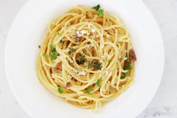 En tallrik med spaghetti, toppad med riven ost, färsk persilja och små bitar av sardeller. Enkel och smakrik pasta med sardeller.