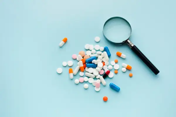 En hög med olika mediciner, kapslar och tabletter, undersöks med ett förstoringsglas.