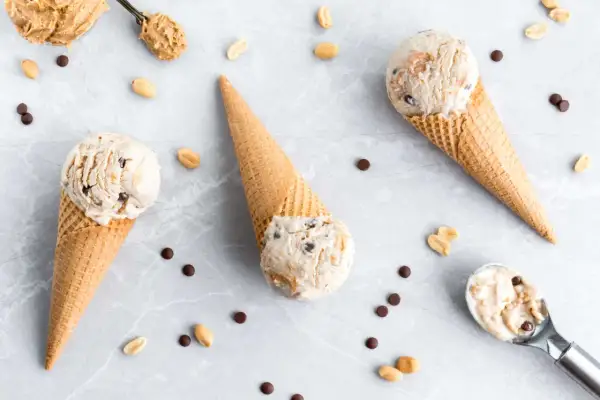 Drei Eiswaffeln mit cremigem Peanut Butter Cup Eis, umgeben von Erdnüssen und Schokostückchen.