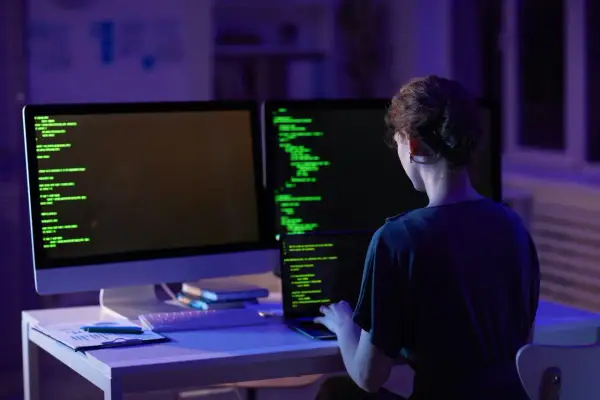 Kobieta programistka pracuje nocą nad kodem. Na ekranach widać zielony tekst, a w pomieszczeniu panuje niebiesko-fioletowe oświetlenie. To jej codzienny crud.