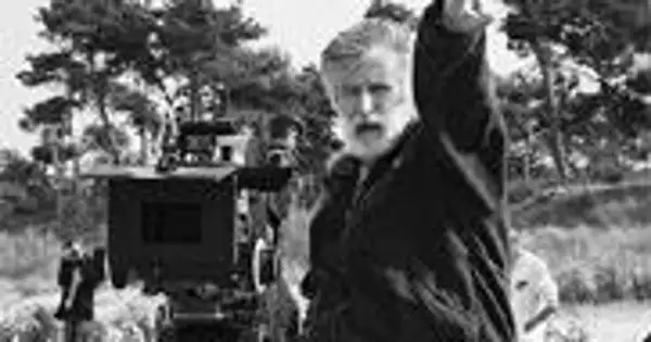 Edward Kłosiński, z siwą brodą, gestykuluje na planie filmowym. W tle widać kamerę i drzewa.
