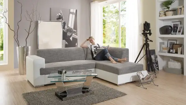 Ein modernes Wohnzimmer mit einer Frau auf dem Sofa, die liest. Der Glastisch davor ist nicht sehr hoch, perfekt für Snacks.