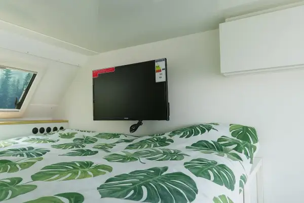 Cama con sábanas de hojas verdes y un televisor de consumo tv 50 pulgadas colgado en la pared.