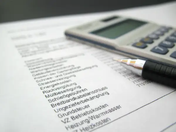 Rechnung mit Stift und Taschenrechner. Liste von Betriebskosten wie Heizung, Grundsteuer und Müllbeseitigung. Ein Widerspruch in der Betriebskostenabrechnung ist möglich.