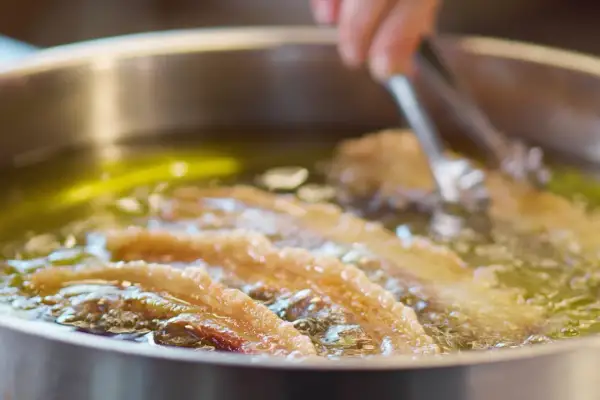 Almitas de Soria dorándose en aceite caliente. Unas pinzas metálicas manipulan la fritura.