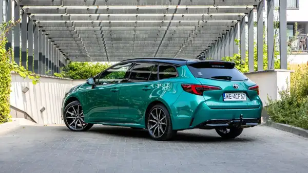 Zielona Toyota Corolla 2.0 Hybrid, kombi, z czarnym dachem, zaparkowana pod nowoczesną pergolą. Dane techniczne tego modelu są imponujące.