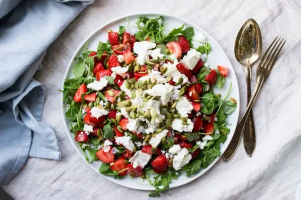 En fräsch sallad med jordgubbar, fetaost och pumpafrön på en vit tallrik.