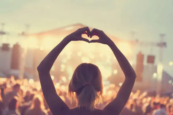 Ragazza fa un cuore con le mani a un concerto, immersa nell'atmosfera delle canzoni romantiche inglesi.