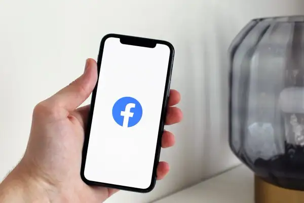 Dłoń trzyma smartfon z logo Facebooka. Dowiedz się, jak wstawić ogłoszenie na FB, by dotrzeć do szerokiego grona odbiorców.