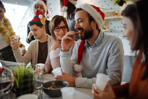 Fröhliche Menschen feiern Weihnachten. Sie tragen Weihnachtsmützen und trinken. Ist Heiligabend ein Feiertag? Ja, und sie genießen ihn!