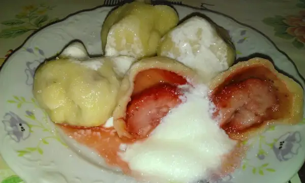 Pyszne pierogi z truskawkami, polane śmietaną i posypane cukrem, kuszą swoim wyglądem i zapachem.