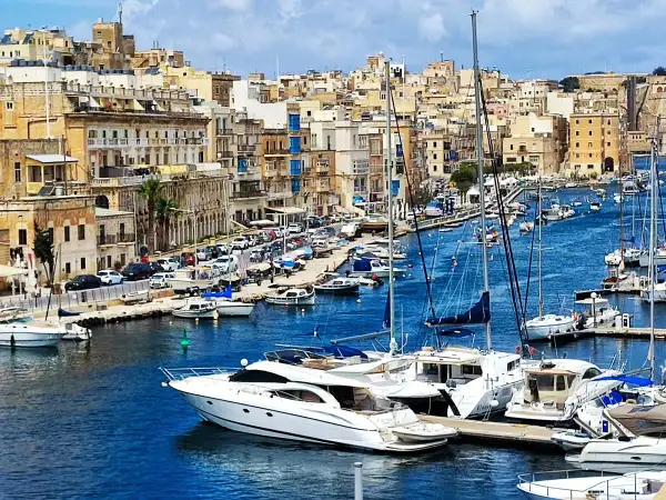 Malta historia: malowniczy port pełen jachtów, z zabytkową zabudową w tle.