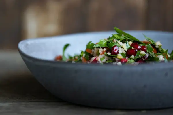 Frischer Tabouleh-Salat mit Granatapfelkernen und Petersilie in einer grauen Schüssel. Ein köstliches Rezept für den Sommer.