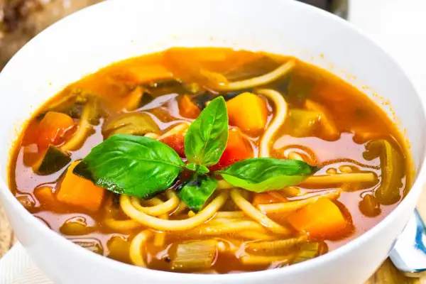 Una ciotola di pasta con i tenerumi, ricca di verdure colorate e basilico fresco. Un piatto confortante e salutare.