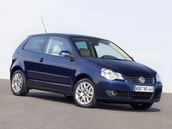 Granatowy Volkswagen Polo 2003, trzydrzwiowy, z jasnym wnętrzem, stoi na szarej nawierzchni.