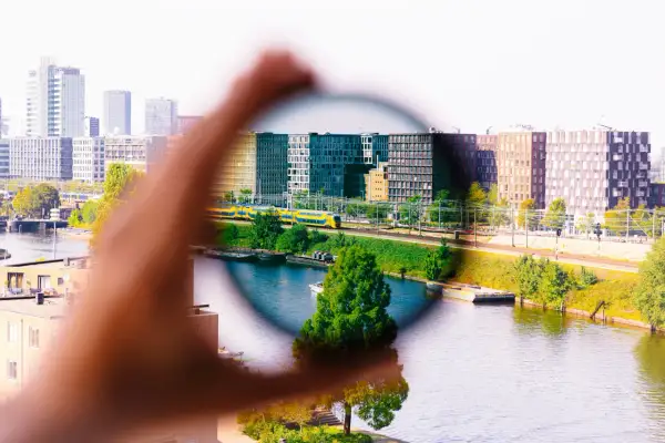 Dłoń trzyma okrągły filtr, przez który widać miasto z pociągiem. Efekt filtrów w fotografii.