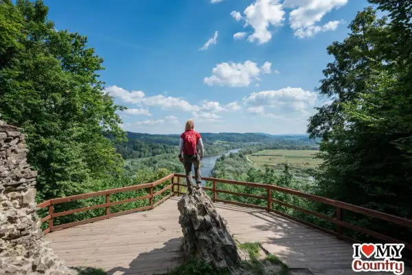 Kobieta z plecakiem podziwia widok na dolinę rzeki. Idealne miejsce, by zastanowić się, gdzie w Bieszczady wybrać się na wędrówkę.