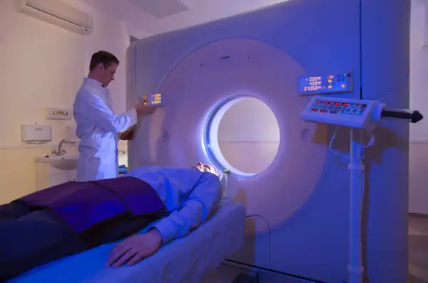 Arzt bedient CT-Scanner, Patient liegt auf Liege. Die CT-Strahlenbelastung wird minimiert.