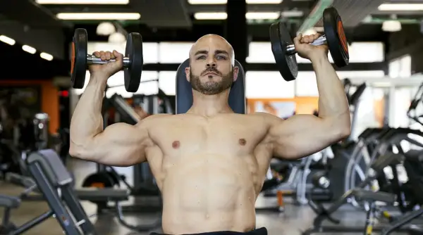 Uomo calvo con barba solleva manubri in palestra, allenamento per il **total body**.