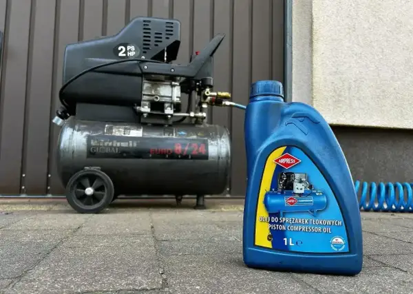 Niebieska butelka z napisem "OLEJ DO SPRĘŻAREK TŁOKOWYCH PISTON COMPRESSOR OIL" obok sprężarki.