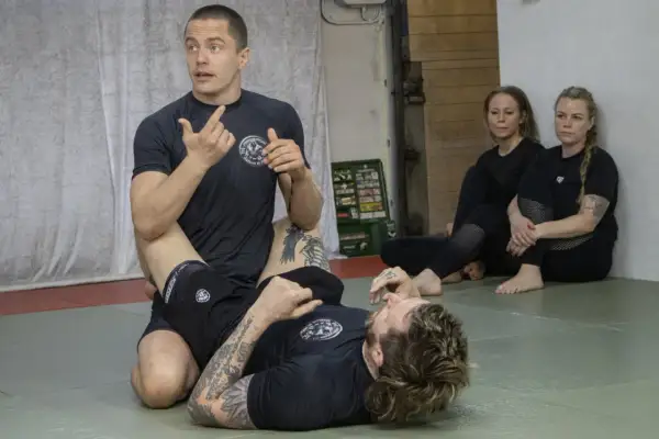 Instruktör visar en teknik i stark bjj. Två kvinnor sitter och observerar.