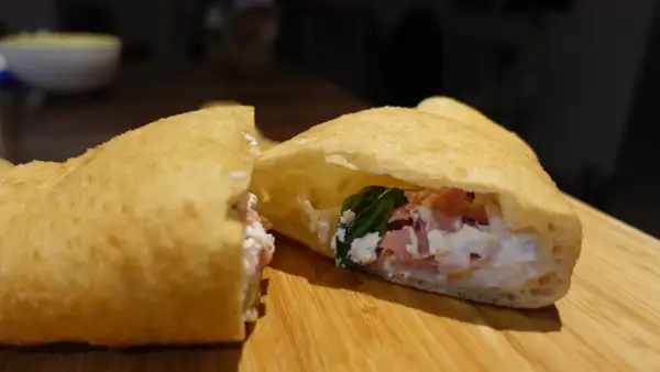 Une pizza frite napolitaine, garnie de ricotta, jambon et basilic, sur une planche en bois.