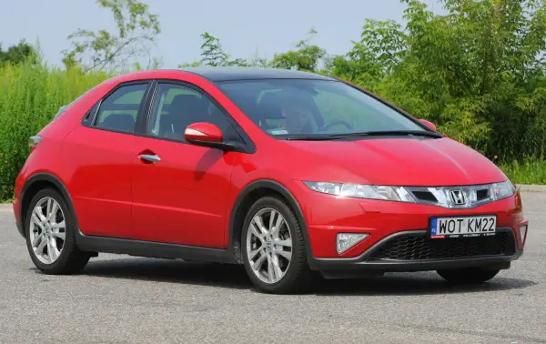 Czerwony Honda Civic 8 z czarnym dachem, zaparkowany na drodze. Widać przednie światła i grill.
