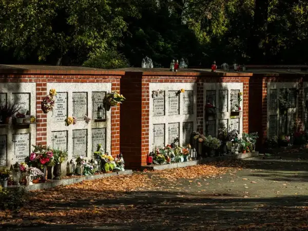 Kamienna ściana na urny z prochami, ozdobiona kwiatami i zniczami, otoczona jesiennymi liśćmi.