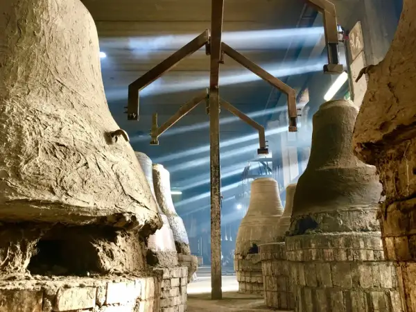 Forni antichi nel paese delle campane Molise, con raggi di luce che illuminano la polvere e le forme grezze delle campane in attesa di essere fuse.