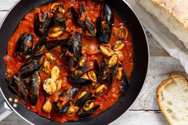 Cozze alla tarantina in padella, un piatto ricco di sapore con cozze succulente in salsa di pomodoro, accompagnate da pane fresco.