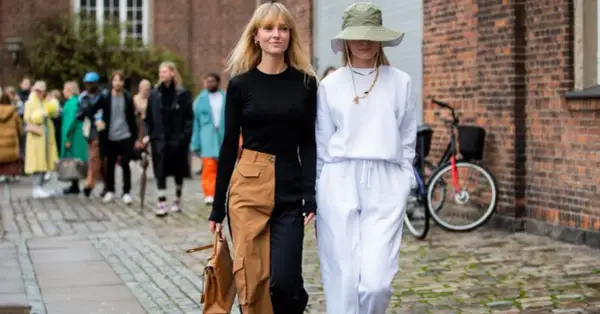Deux femmes marchent, l'une porte un pantalon bicolore audacieux, l'autre un ensemble blanc décontracté.